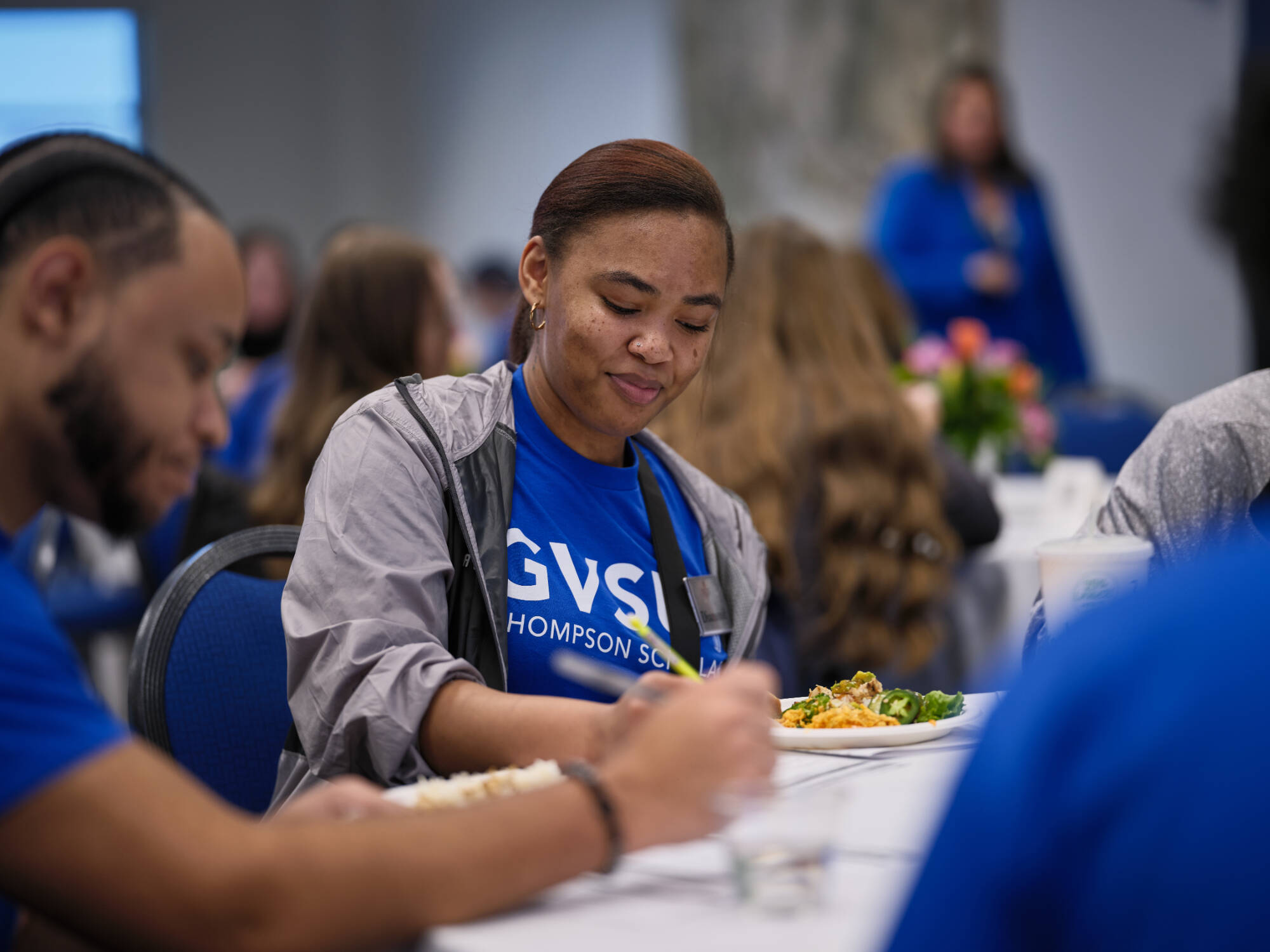 Students sitting at a table, wearing blue Thompson Scholar shirts, taking notes.